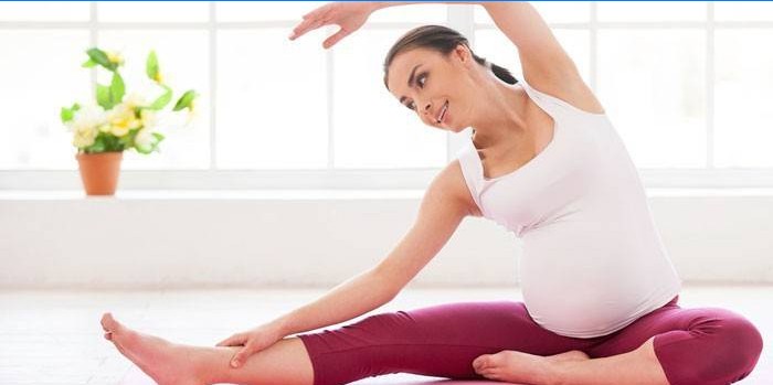 Gravid pige gør øvelser derhjemme.