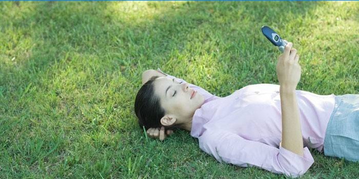 Pigen ligger i græsset med en telefon