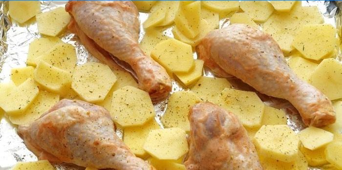 Kartoffelskiver og kyllingetrommelstikker på en bageplade inden bagning
