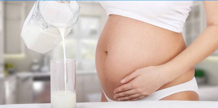 Gravid kvinde hælder gæret bagt mælk i et glas