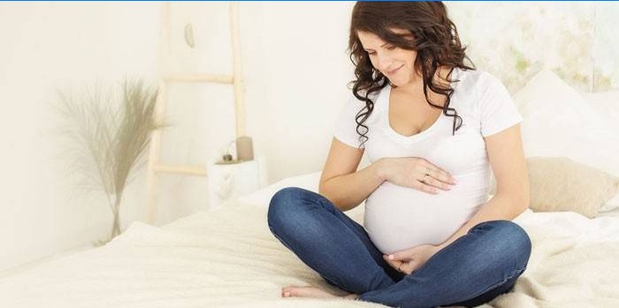 Gravid kvinde sidder på sengen