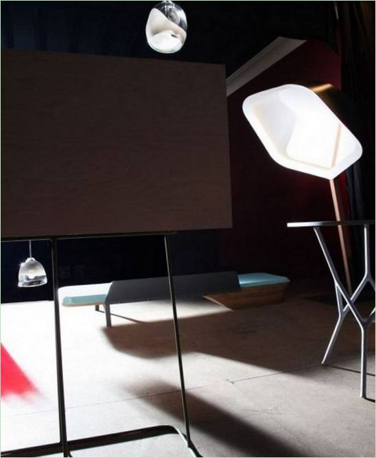 En sammensætning af husholdningsgenstande: en skrivebordslampe, hængelamper, et bord med gennembrudte ben, en daybed i træ og et skrivebord